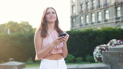 Joyful Pretty Caucasian Young Woman Texting on Smartphone While Walking in Town Beautiful Girl