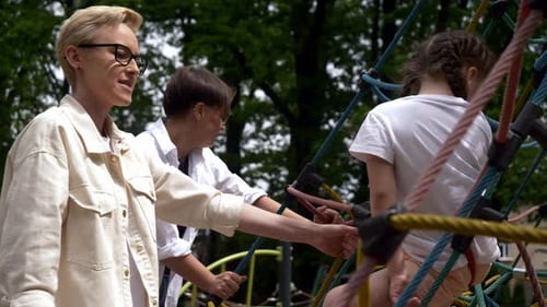 Eine verspielte Tochter klettert in Begleitung ihrer lesbischen Mütter furchtlos auf dem Spielplatz auf das Netz, en