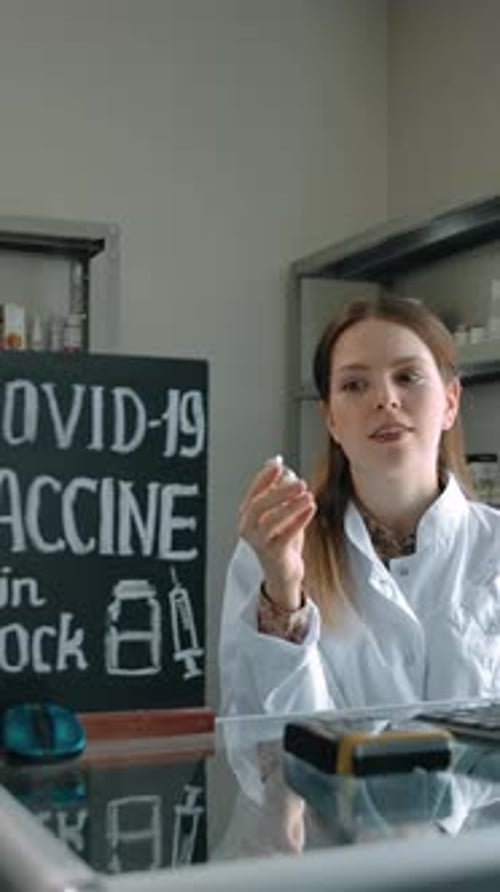 Vertical of Pretty Caucasian Woman Pharmacist Presents New Covid19 Vaccine in Stock