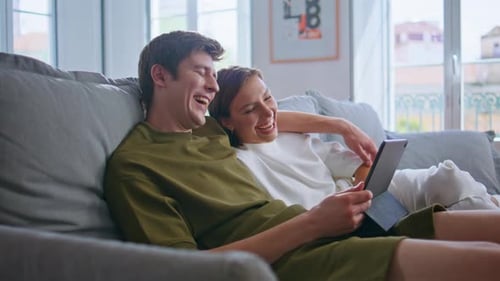 Couple Relaxing on Sofa Laughing at Tablet Together