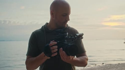 Man Holds Camera on Beach at Sunset