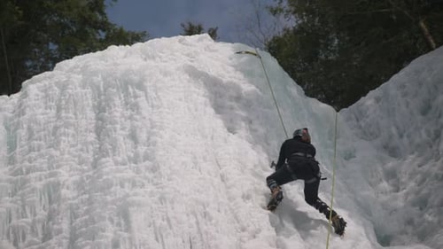 An adventure ice climber attempts to scale a sheer ice covered rock face