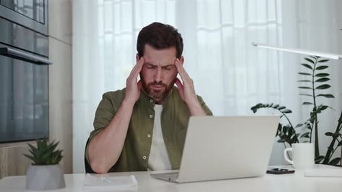 Stressed Man at Computer Rubbing Temples Indoors