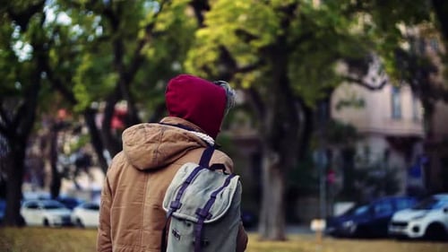 A Rear View of Homeless Beggar Man Walking Outdoors in City Looking
