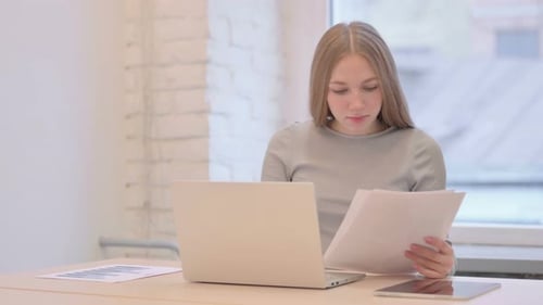 Young Woman Works with Laptop and Documents at Desk