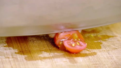 Male cutting a red cherry tomato with a very sharp silver knife on a wooden cutting board. Close up