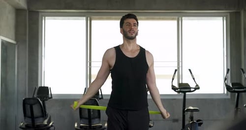 Adult male athlete stands smiling in modern gym, holding green resistance band after strength