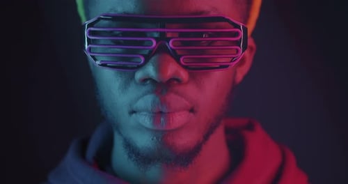 Closeup of African American Man Raising Head Wearing Neon Illuminated Glasses on Dark Background