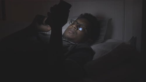 Young Man Using Smart Phone at Night on Bed