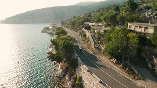 Car with SUP Board on Roof Drives Along Road on Cliff