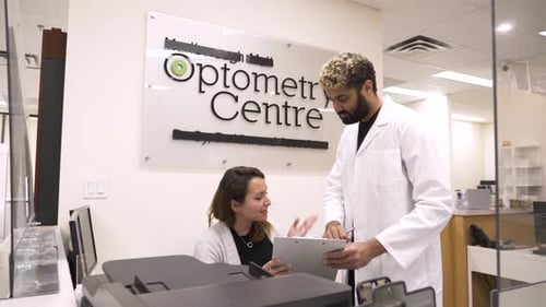 Optometrist and receptionist discuss paperwork at optometry center front desk