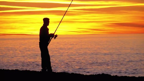 Silhouette of a Fisherman with a Fishing Rod at Sunset Over the Sea