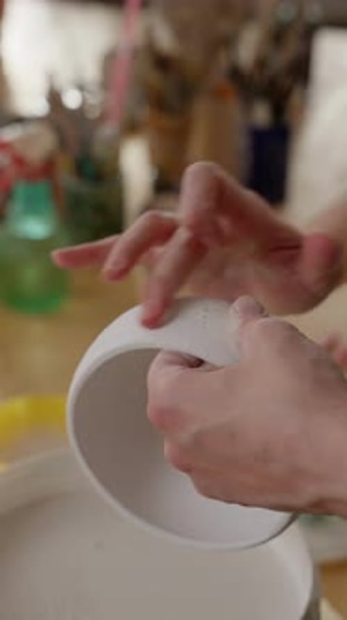 Hands Applying Liquid to Ceramic Bowl in Studio