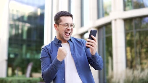 Excited Man Celebrating Success on Smartphone Outdoors