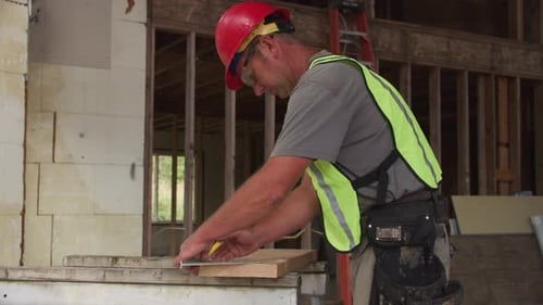 Construction Worker Measuring and Cutting Lumber on Site