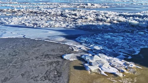Große Eisschollen und -platten, die eine Wasseroberfläche bedecken, bilden einen strukturierten Hintergrund in der Luftaufnahme