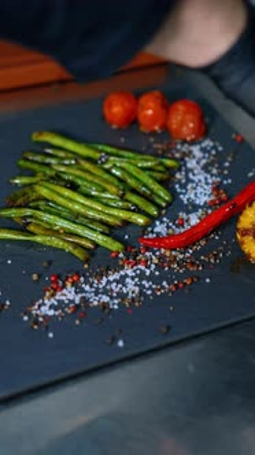 Cook puts the fried vegetables on the black charcuterie board. Serving the dish. Close up.