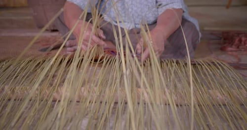An Asian female farmer who is an elderly native basketry artisan weave mat from bamboo