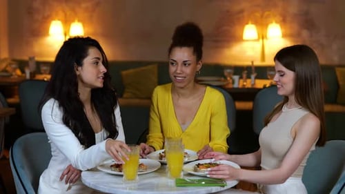 Happy Young Girlfriends Having Dinner in a Restaurant and Clinking Glasses with a Cocktails Meeting