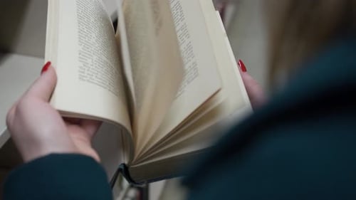 A woman reading a book in a library while quickly flipping through the pages