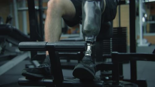 Athlete with Prosthesis on Leg Trains on Machine in Gym
