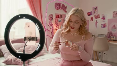 Joven rubia filmando un blog de belleza en su habitación de temática rosa