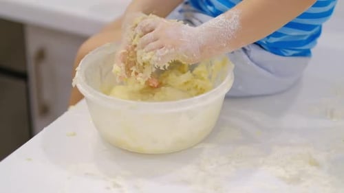 Child Mixes Dough with Hands in Kitchen Bowl