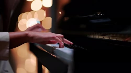 Close up of a woman's hands playing the piano with blurry lights on the background