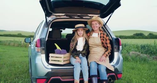 Mother and Daughter with Flowers in Car Trunk