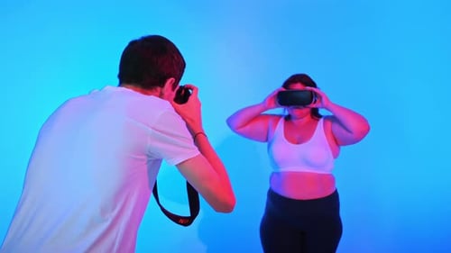View of a photographer taking portraits of a woman with overweight in a tracksuit and VR headset in