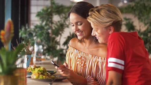 Hispanic friends enjoying lunch at a restaurant using a smartphone for social media