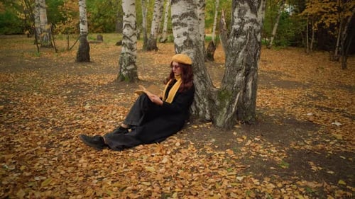 Stylish Lady in Solitude Relaxing Against Tree Reading Book in Autumn Forest
