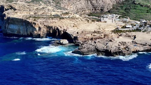 Azure Mediterranean Waves Crashing Against Rugged Limestone Cliffs Of Dwejra Bay Under Golden