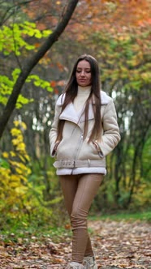 Relaxed long-haired brunette tossing fallen leaves walking by the road.