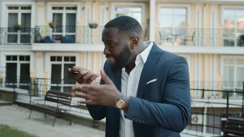 Irritated african american businessman gesturing during video call on urban street