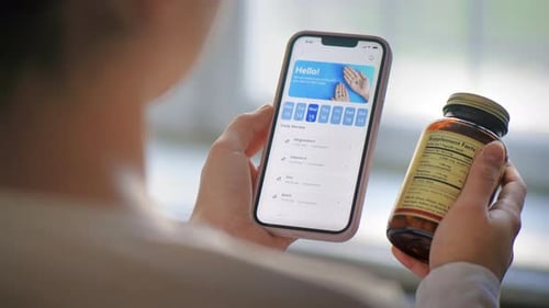 Close view of a person using smartphone with medication tracker app holding a jar of pills