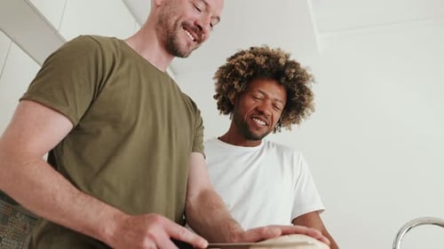 Two Men Smiling Together Cutting Bread in Kitchen