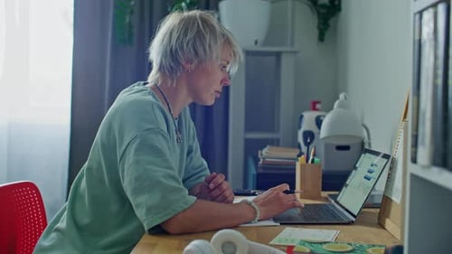 Concentrated Woman Working on Laptop and Taking Notes at Desk in Home Office