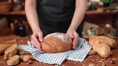 Bäckerin in schwarzer Schürze legt frisch gebackenes Brot auf den Tisch einer kleinen Hausbäckerei, Nahaufnahme