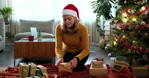 Woman Wrapping Christmas Presents at Home by Tree