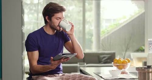 Man Using Tablet While Drinking Beverage in Kitchen