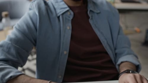 Programador masculino de Oriente Medio con auriculares escribiendo en el teclado en la oficina