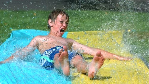 Excited Boy Slides Down Colorful Wet Backyard Slide