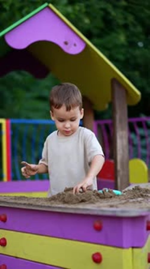 Jeune garçon jouant dans un bac à sable avec du sable en le touchant avec ses mains.