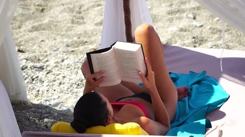 Woman Reading Book Lies on the Beach Chair Under Beach Umbrella on Vacation Summer Holidays Travel