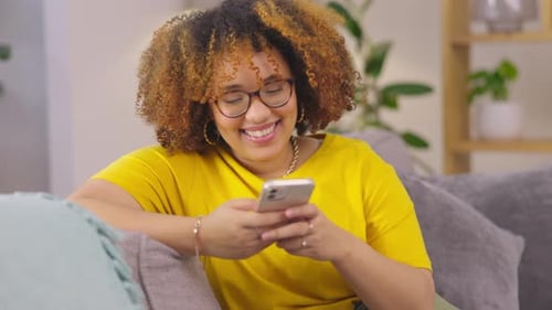 Woman Smiling While Using Smartphone on Couch