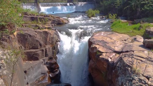 Beauty of the waterfall, surrounded by brown stones and green grass, sunny weather, dolly shot