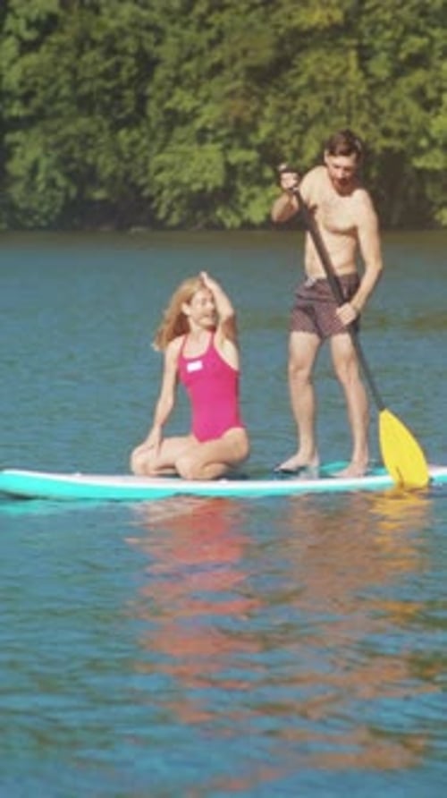 Journée ensoleillée avec équilibre ludique sur l'eau en couple faisant du paddleboard sur le lac pendant un été ensoleillé
