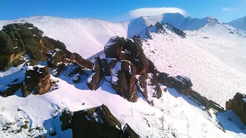 Beautiful winter rocks against the backdrop of snow-capped mountains and sunny blue sky from a drone