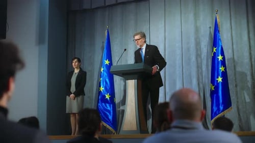 Man Speaking at Podium With Flags On Stage